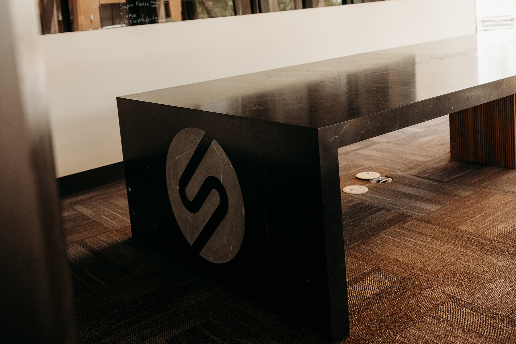 Full Custom direction: completed black stone boardroom table with the client logo inlaid in contrasting stone on the waterfall end panel