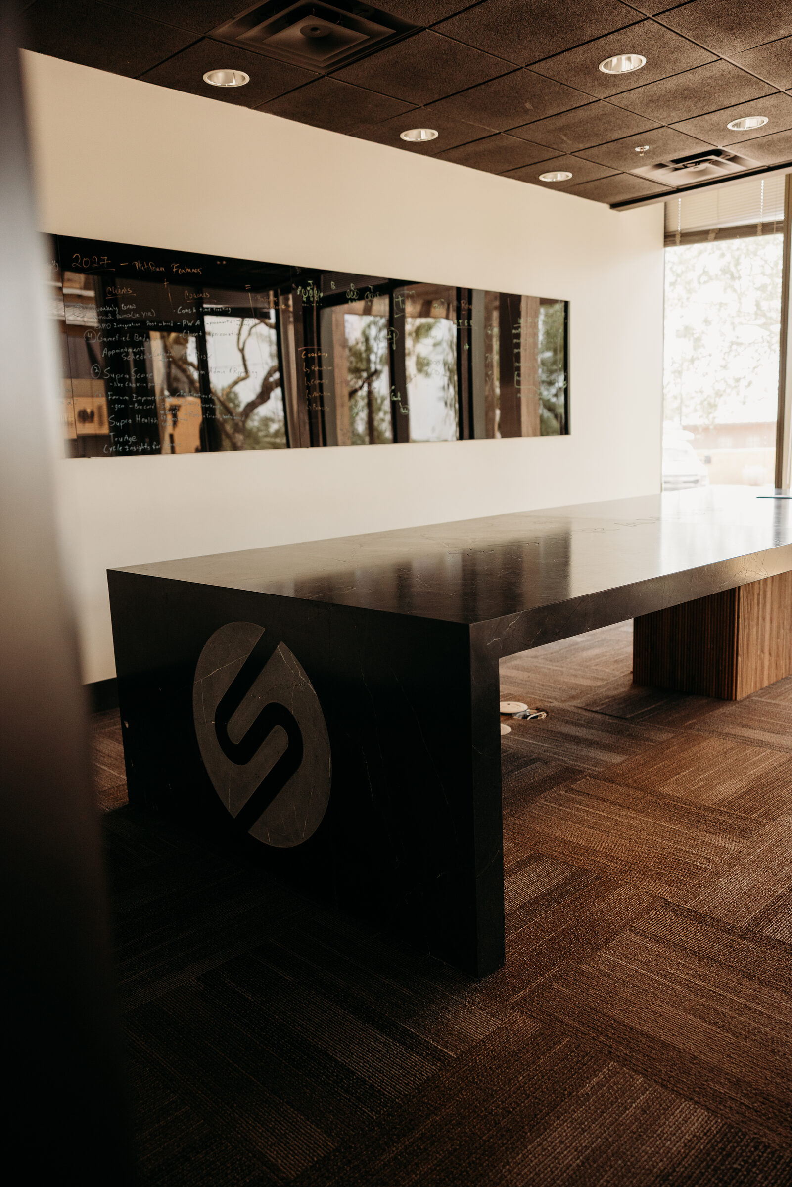 Custom executive boardroom table in Arizona with a black marble top, stone waterfall end panel and solid wood base along a window wall